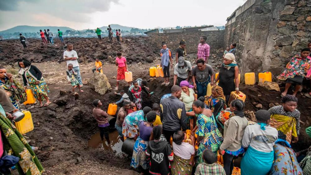 Residents gather around a water point in a lava-covered field in Goma. — AFP