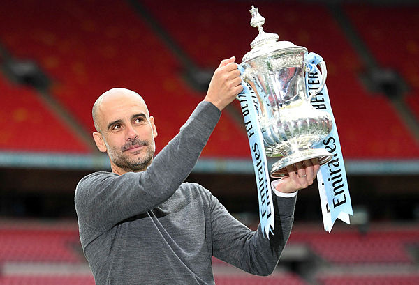 Manchester City’s Spanish manager Pep Guardiola holds the winner’s trophy as the team celebrates victory after the English FA Cup final football match between Manchester City and Watford at Wembley Stadium in London, on May 18, 2019. - AFP