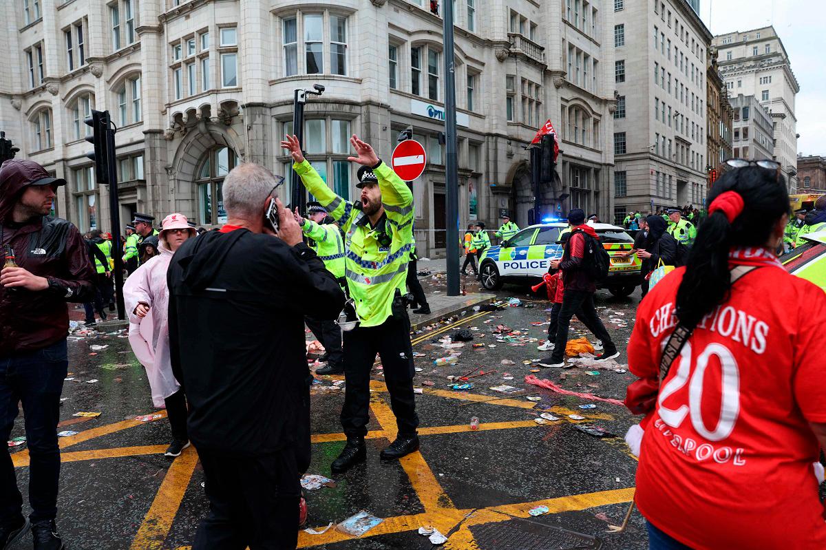 A Police officer shouts at Liverpool fans as he stands on duty a t a Police cordon at the entrance to Water Street, at the scene of an incident, on the sidelines of an open-top bus victory parade for Liverpool’s Premier League title win, in Liverpool, north-west England on May 26, 2025. - Darren Staples / AFP