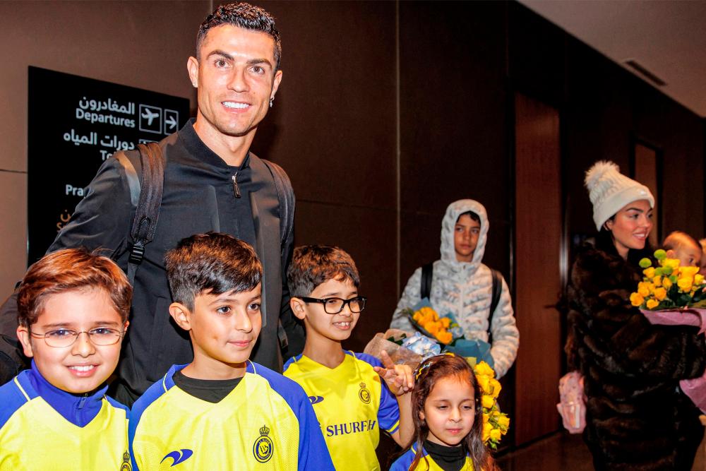 A handout taken and released by Al Nassr football club on January 2, 2023 shows Portugal’s Cristiano Ronaldo (L) posing for picture with Saudi children as his son Cristiano Ronaldo Jr (C) and partner Georgina Rodriguez (R) stand by, upon arrival at a private airport in Riyadh, on the eve of his grand unveiling before thousands of fans at Saudi Arabia’s Al Nassr club, after sealing a shock move estimated at more than 200 million euros/AFPPix