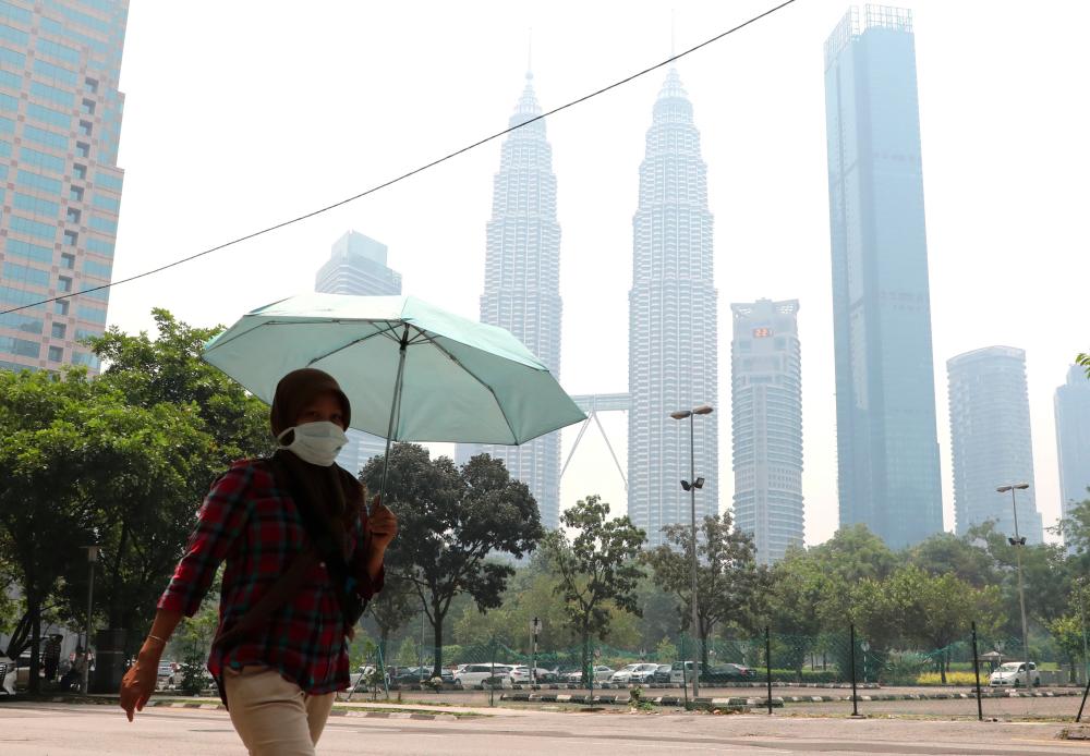 A woman wears a mask as Petronas Twin Tower is shrouded in haze in Kuala Lumpur, Sept 11, 2019. - Reuters