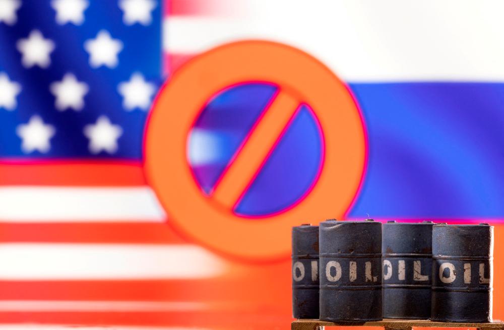 Models of oil barrels are seen in front of a displayed ‘stop’ sign, US and Russia flag colours in this illustration. – Reuterspic