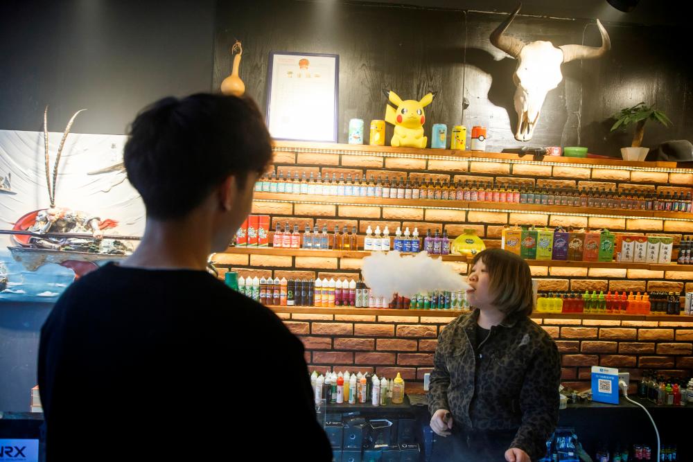A saleswoman exhales vape as she talks to a customer at the Vape Shop that sells e-cigarette products in Beijing, China January 30, 2019. - Reuters