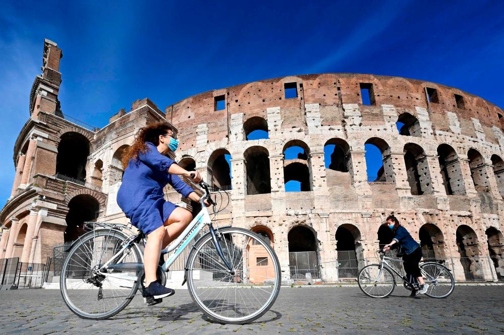 In this file photo taken on May 8, 2020 shows women ride a bicycle past the Colosseum monument in Rome on May 8, 2020, during the country’s lockdown aimed at curbing the spread of the Covid-19 infection, caused by the novel coronavirus. — AFP