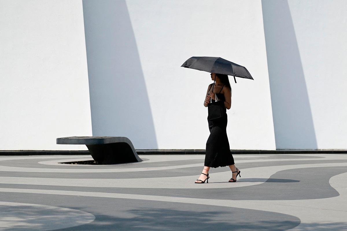 A woman holding an umbrella to shelter from the sun walks along a street in Beijing on June 23, 2025 - WANG Zhao / AFP