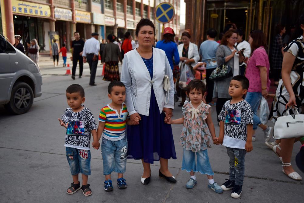 This file photo taken on June 4, 2019 shows a Uighur woman waiting with children on a street in Kashgar in China’s northwest Xinjiang region. — AFP