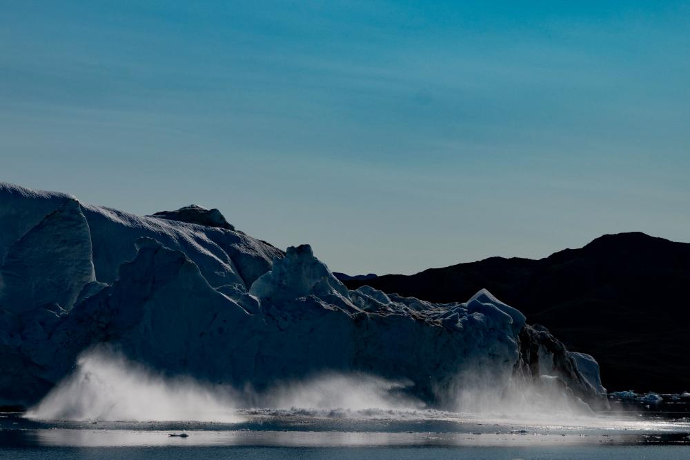 (FILES) Pieces of a melting iceberg collapse into the sea in Scoresby Fjord, Greenland on August 15, 2023. - AFPPIX