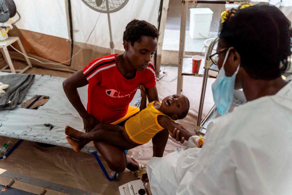 (FILES) In this file photo taken on October 07, 2022, a woman holds a child showing symptoms of cholera while he receives treatment at a clinic run by Doctors Without Borders in Cité Soleil. AFPPIX
