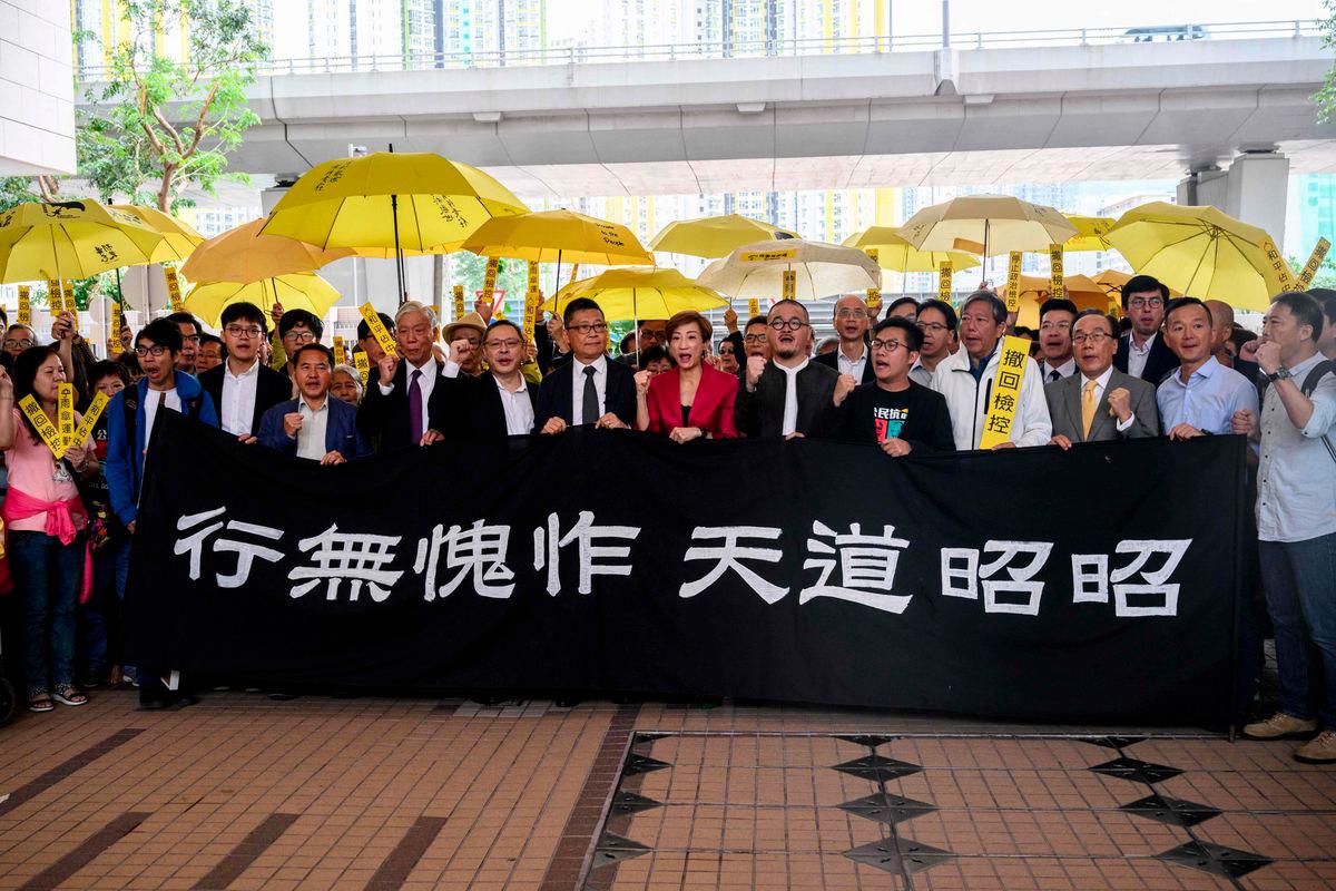 (L-R behind banner) Pro-democracy activists Chung Yiu-wa, Cheung Say-yin, former Democratic Party lawmaker Lee Wing-tat, baptist minister Chu Yiu-ming, 74, law professor Benny Tai, 54, sociology professor Chan Kin-man, 59, lawmakers Tanya Chan and Shiu Ka-chun, and League of Social Democrats vice-chairman Raphael Wong, chant before entering the West Kowloon Magistrates Court in Hong Kong on November 19, 2018. - AFPPIX