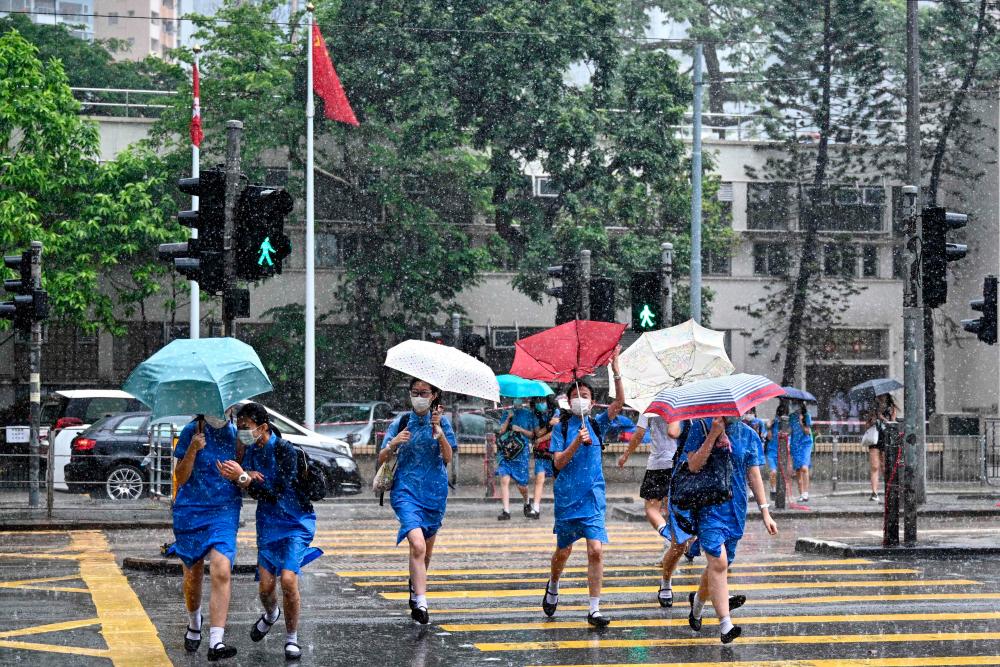 In this file picture taken on July 8, 2020, students run for shelter during a sudden but brief heavy downpour in Hong Kong. China's new security law has sent a chill through Hong Kong's schools and universities with many teachers fearful the city's reputation for academic freedom and excellence is now at risk. — AFP
