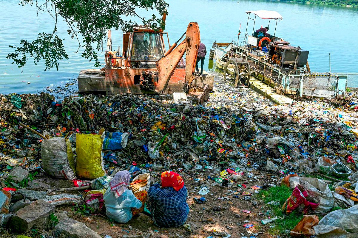 Ragpickers sit near the plastic waste gathered at Hussain Sagar lake in Hyderabad on September 14, 2024. - AFPPIX