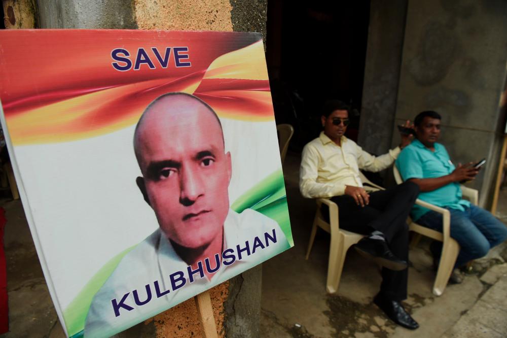 Indian residents sit next to a placard with the picture of Kulbhushan Jadhav, an Indian national convicted of spying in Pakistan, in the neighborhood where he grew up, in Mumbai. — AFP