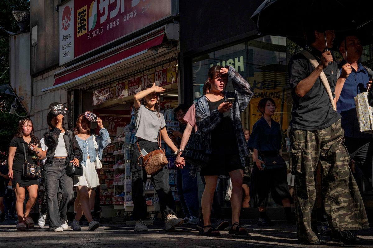 People shield their eyes from the sun as they walk through a street on a hot day in Tokyo on July 26, 2025. - AFPPIX