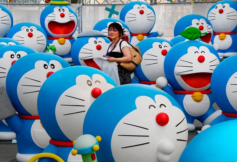 (FILES) This picture taken on July 18, 2013 shows a journalist walking amid life-size figures of Doraemon during the press preview of the Fujiko F Fujio Exhibition in Tokyo. A Japanese actress who was the voice of “Doraemon”, a cartoon cat robot beloved by children in Japan and other countries has died, her agency said on October 11, 2024. She was 90. - TORU YAMANAKA / AFP