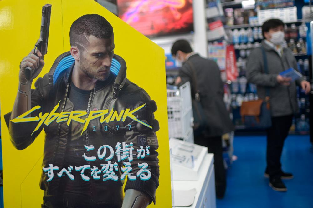 (FILES) This file photo taken on December 18, 2020 shows an advertisement for the Cyberpunk 2077 video game for the Sony Playstation, as shoppers browse the gaming section of a shop in Tokyo. Troubled game Cyberpunk 2077 will return to PlayStation stores from next week, Sony confirmed on June 16, 2021, six months after it was pulled over bugs and compatibility issues. – AFP