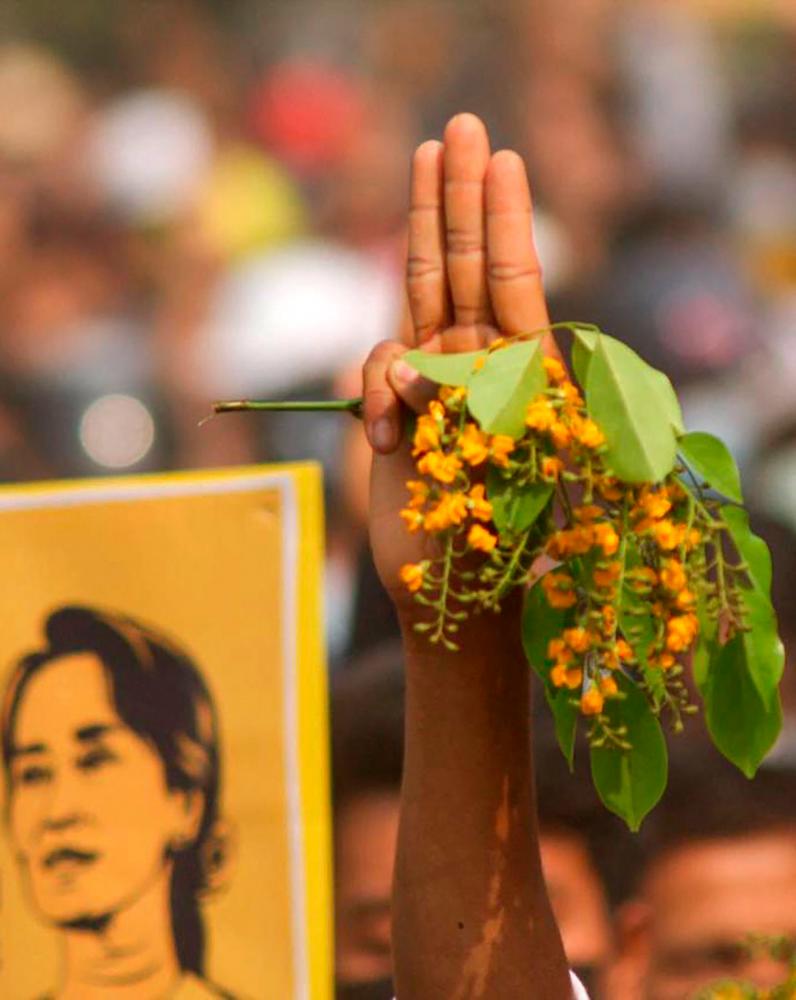 (FILES) This file photo taken and received from an anonymous source via Facebook on April 1, 2021 shows a protester making the three-finger salute while holding padauk flowers, which usually bloom during Myanmar's New Year Thingyan festival, during a demonstration against the military coup in Monywa in the Sagaing region. –AFP