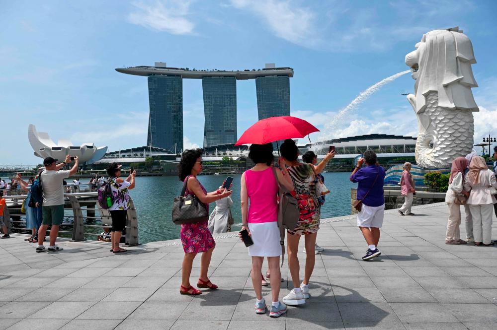 (FILES) In this file photo taken on April 24, 2023 people take pictures next to the Merlion Statue at Marina Bay in Singapore. The temperature in Singapore hit 37 degrees Celsius (98.6 Fahrenheit) on May 13, matching the city-state’s 1983 record. - AFPPIX