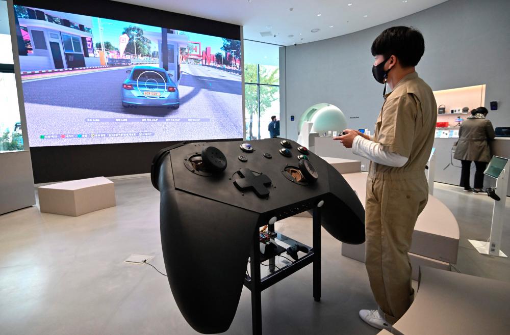 (FILES) In this file photo taken on November 09, 2020 A staff member plays a game in front of an oversized mock-up of Microsoft's Xbox controller at a flagship store of SK Telecom in Seoul on November 10, 2020. – AFP