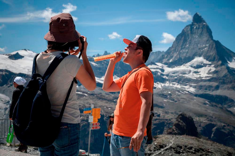 (FILES) This file photograph taken on August 8, 2020, shows a tourist posing while holding a Swiss chocolate bar of the brand Toblerone, owned by US food giant Mondelez International at the Gornergrat, with the Matterhorn mountain in background, 3’089 meter hight above the resort of Zermatt. AFPPIX