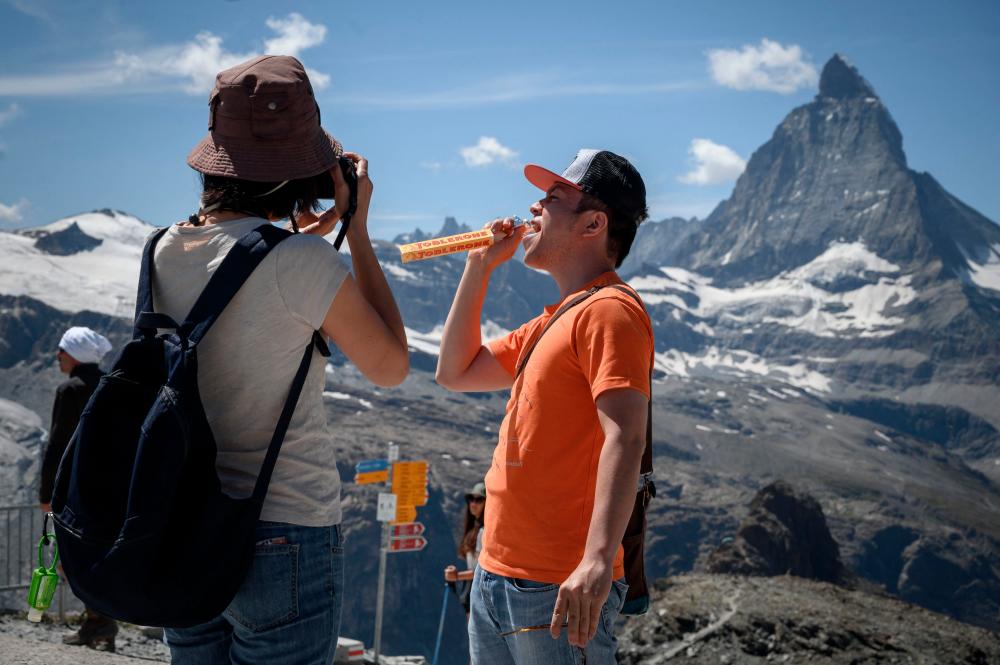 (FILES) This file photograph taken on August 8, 2020, shows a tourist posing while holding a Swiss chocolate bar of the brand Toblerone, owned by US food giant Mondelez International at the Gornergrat, with the Matterhorn mountain in background, 3’089 meter hight above the resort of Zermatt. AFPPIX