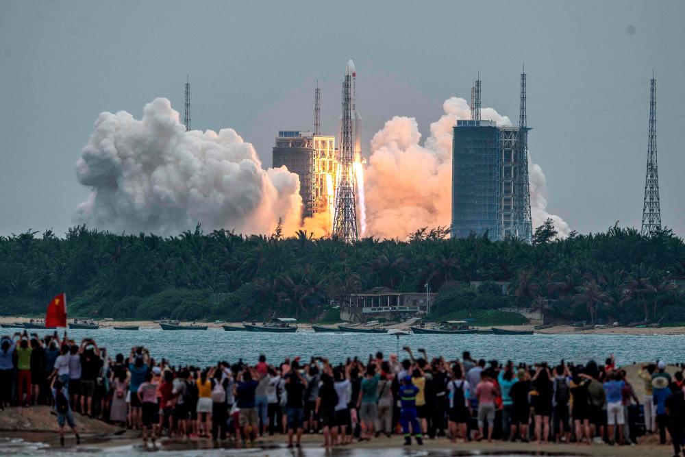 (FILES) In this file photo taken on April 29, 2021 People watch a Long March 5B rocket, carrying China’s Tianhe space station core module, as it lifts off from the Wenchang Space Launch Center in southern China’s Hainan province. -AFP