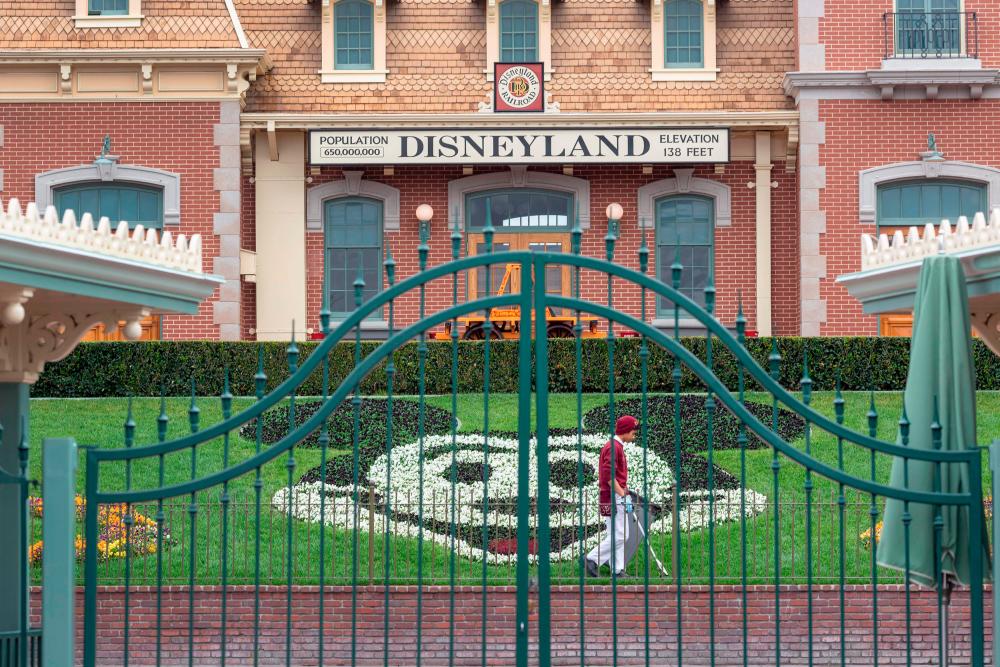 (FILES) In this file photo taken on March 14, 2020 an employee cleans the grounds behind the closed gates of Disneyland Park on the first day of the closure of Disneyland and Disney California Adventure theme parks as fear of the spread of coronavirus continue, in Anaheim, California. Disney announced September 29, 2020, it will cut 28,000 jobs from its US parks and experiences division, pointing to depressed demand caused by the coronavirus and uncertainty on when it will recover. / AFP / DAVID MCNEW