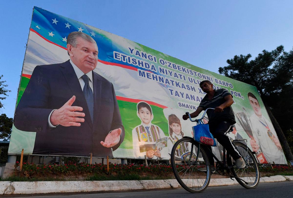 (FILES) A man rides a bicycle in front of a banner displaying Uzbek President Shavkat Mirziyoyev in the center of Termez near the Uzbek-Afghan border about 700 km from Tashkent, on August 15, 2025. Prisoners in Uzbekistan will be able to plead for reduced sentences if they read books selected by authorities to cultivate “correct spiritual and moral values”, officials said. (Photo by Vyacheslav OSELEDKO / AFP)