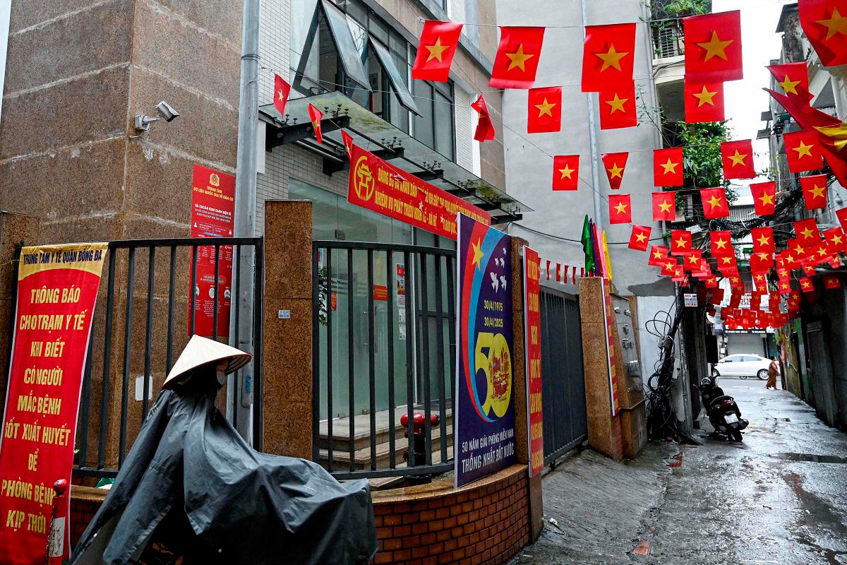 (FILES) A woman wearing a raincoat walks with her bicycle past a former local authorities’ building which closed due to Vietnam’s new administrative structure of 34 provinces and cities in Hanoi on July 1, 2025. - AFPpix
