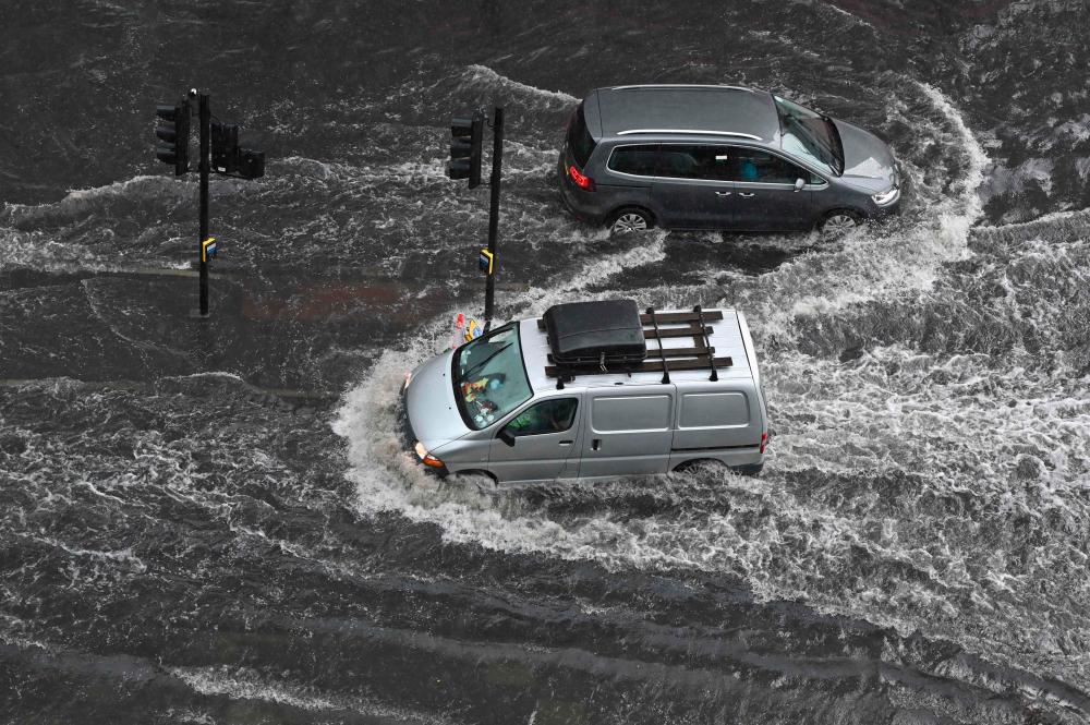TOPSHOT - Vehicles drive through deep water on a flooded road in The Nine Elms district of London on July 25, 2021 during heavy rain. Buses and cars were left stranded when roads across London flooded on Sunday, as repeated thunderstorms battered the British capital. -AFP