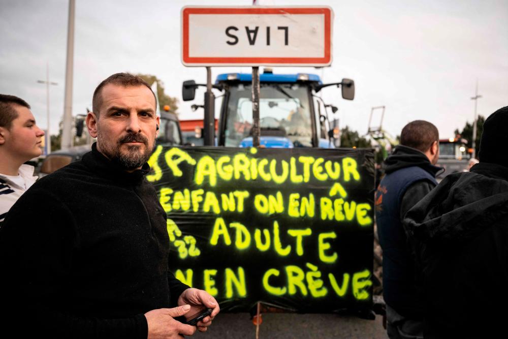 Farmers gather next to a tractor displaying a message which reads as “Farmer, as a kid we dream of it, as an adult we die of it” and an upside down roadsign, as tractors block the entrance of the Toulouse-Blagnac airport in Toulouse, southwestern France on January 30, 2024/AFPPix