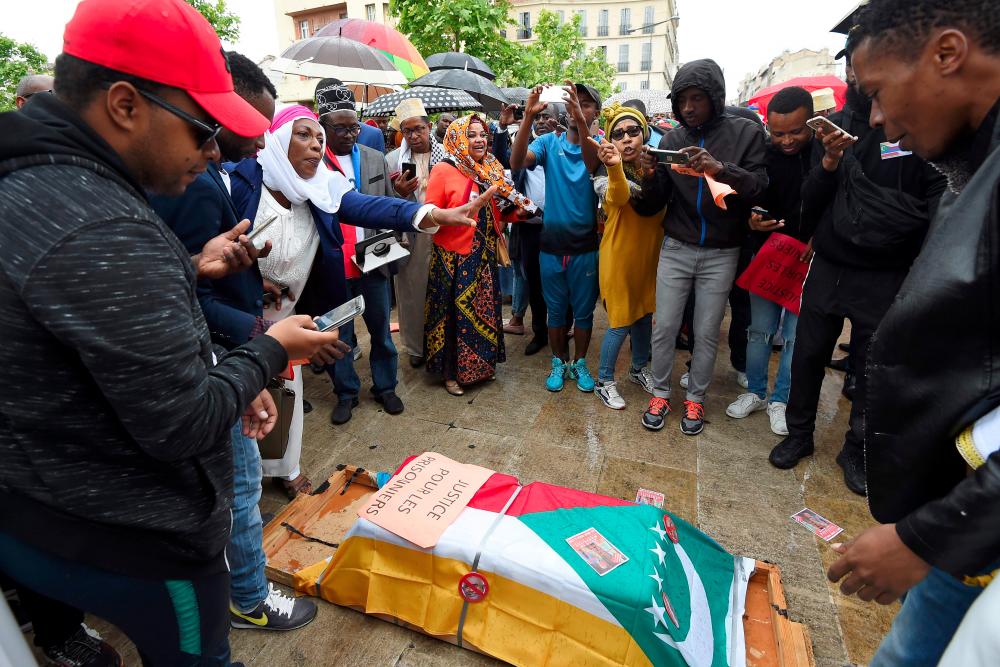 Comorian opponents of the new elected President Azali Assoumani stands around a fake coffin covered with a Comorian national flag and a placard reading justice for the prisoners during a protest on May 26, 2019 in Marseille, southern France. — AFP