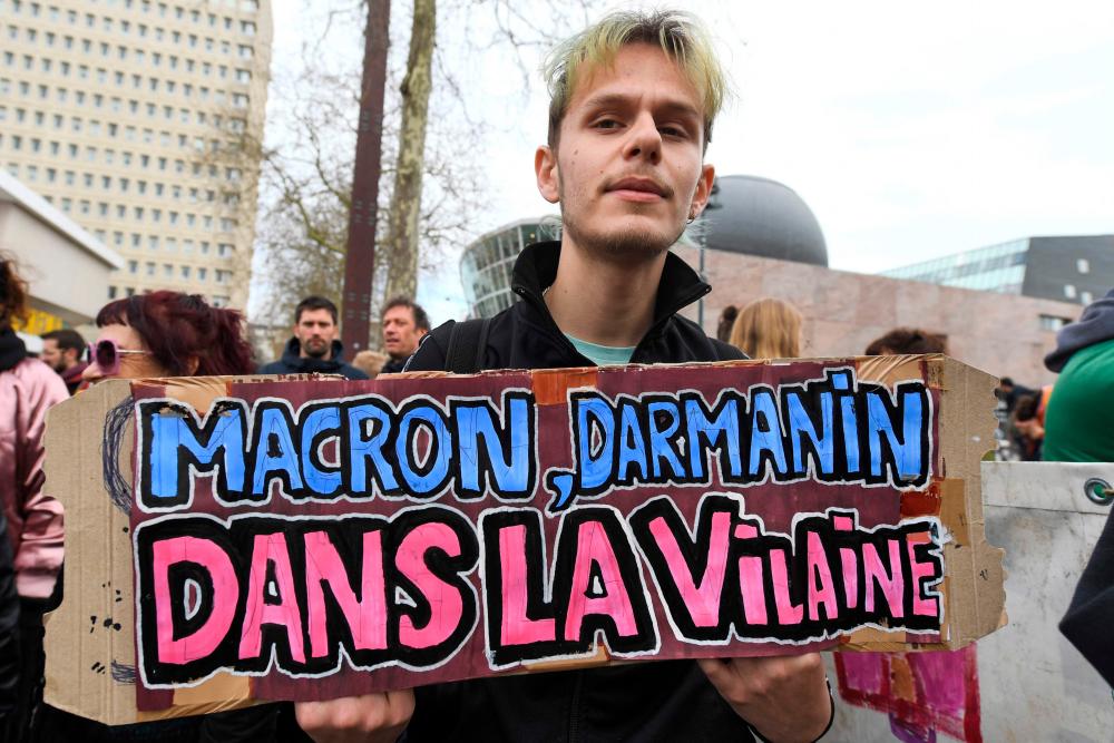 A man holds a sign reading “Macron, Darmanin, in the Vilaine (a river)” during a protest against the Darmanin legislative proposal on immigration and the administrative detention centres in Rennes, western France on March 25, 2023. AFPPIX