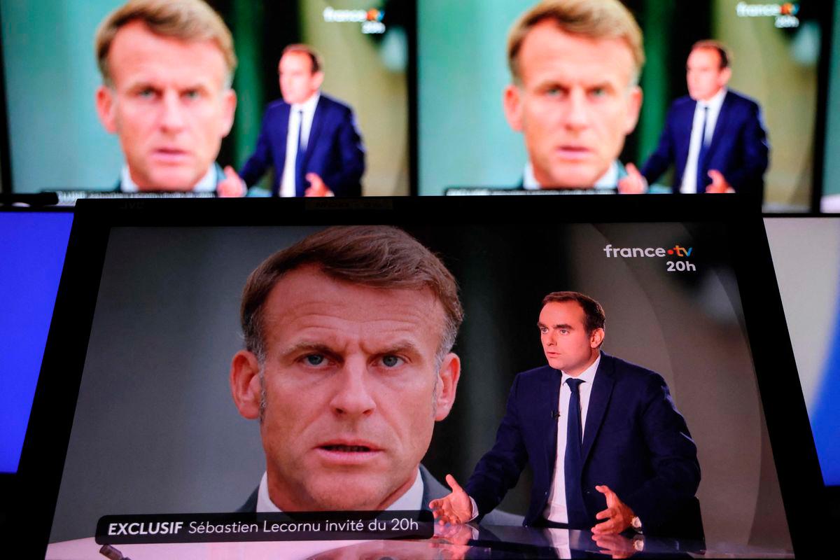 This photograph shows a television screen displaying France’s outgoing Prime Minister Sebastien Lecornu (R), with an image of France’s President Emmanuel Macron in the background, during a live broadcast interview on a set of French TV France 2 in Paris on October 8, 2025. (Photo by Ludovic MARIN / AFP)