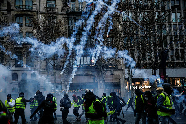 Protesters wearing yellow vests (gilets jaunes) stand amid smoke of tear gas during a demonstration against rising costs of living they blame on high taxes on the Champs-Elysees avenue in Paris, on Dec 15, 2018. — AFP