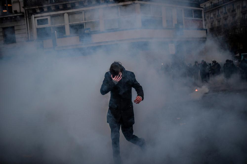 A man covers his eyes as he tries to find his way amid heavy smoke during clashes between anti-riot police and protestors during a demonstration against the pension overhauls, in Paris, on Dec 5, 2019 as part of a national general strike. — AFP