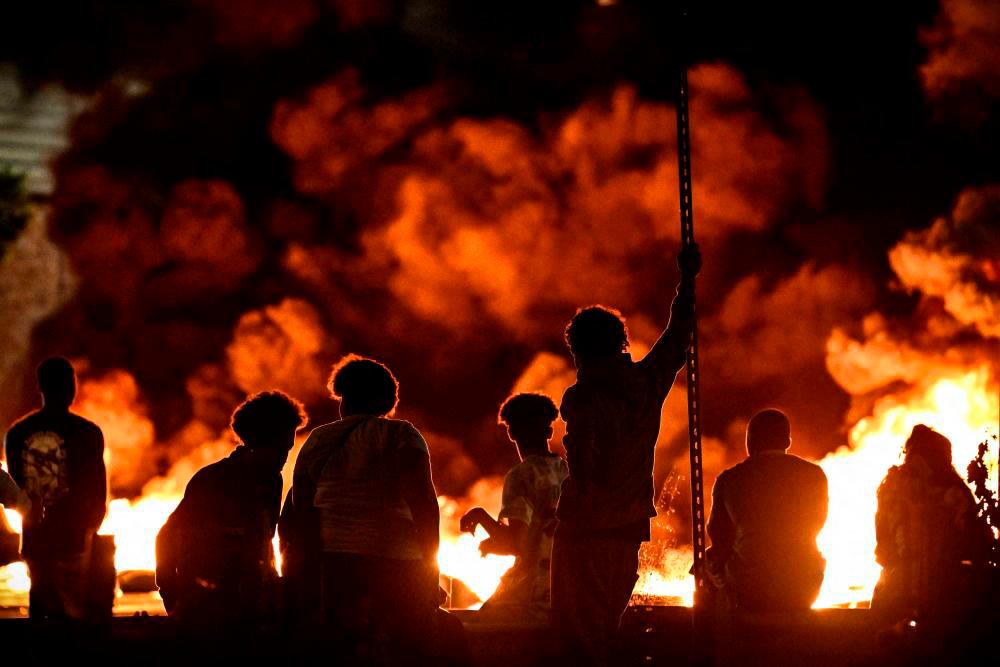 TOPSHOT - People look at burning tyres blocking a street in Bordeaux,, south-western France on late June 29, 2023, during riots and incidents nationwide after the killing of a 17-year-old boy by a police officer’s gunshot following a refusal to comply in a western suburb of Paris. - AFPPIX