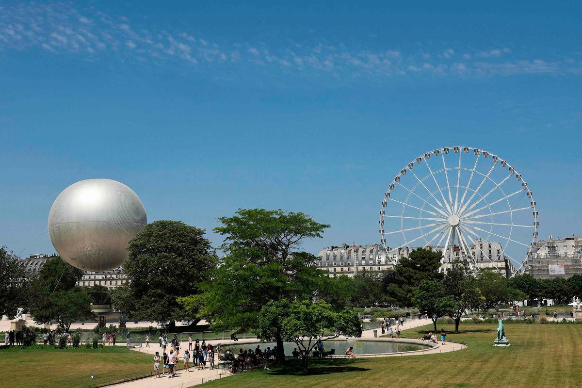 People walk pass by the Olympic Cauldron (L) and the Giant Ferris Wheel (R) at the Tuileries Garden, during a hot summer afternoon, in Paris, on June 19, 2025-AFP