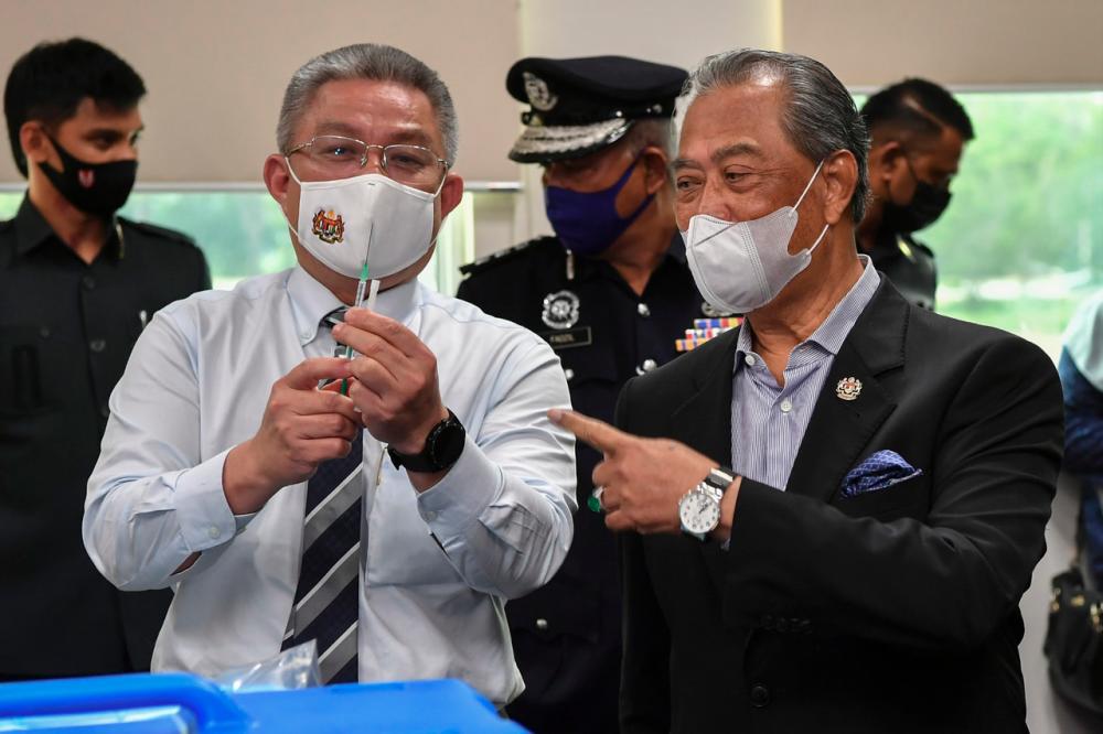 Prime Minister Tan Sri Muhyiddin Yassin watching Health Minister Datuk Seri Dr Adham Baba demonstrate how to use the Low Dead Volume (LDV) syringe- Bernama