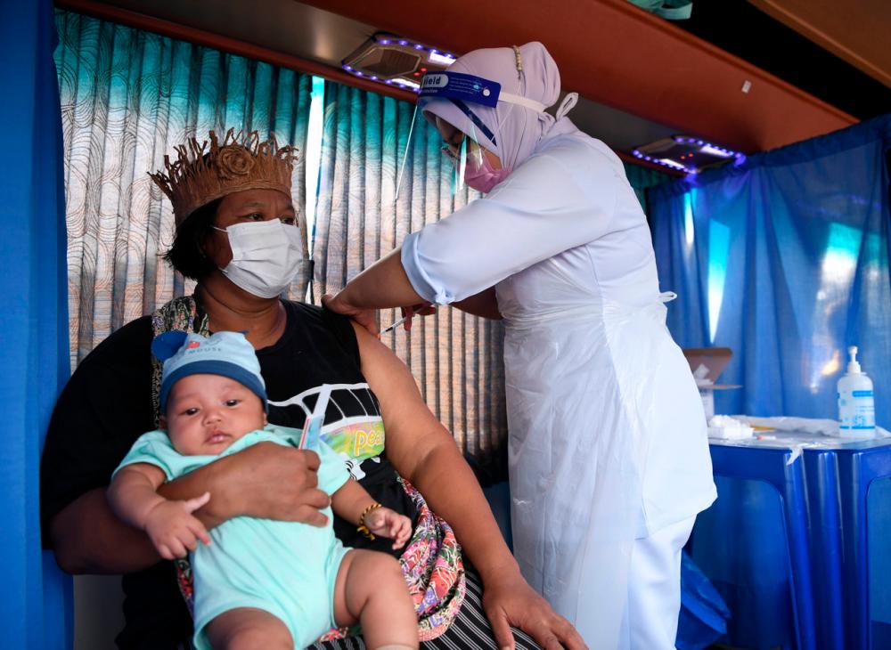An Orang Asli lady by the name of Norhayati Tukol is being vaccinated while holding her child in Banting.