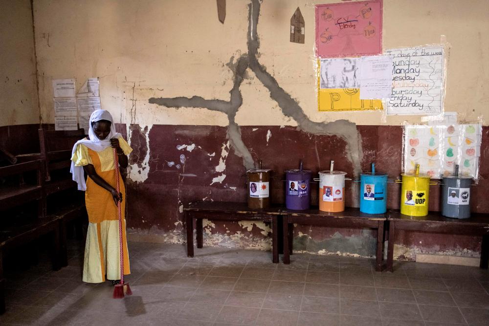 A volunteer cleans a voting station inside a school in the neighbourhood of Manjai Kunda, on the eve of the presidential election in Banjul on December 3, 2021. Gambia is the only country to vote using marbles, inserted into drums. AFPpix