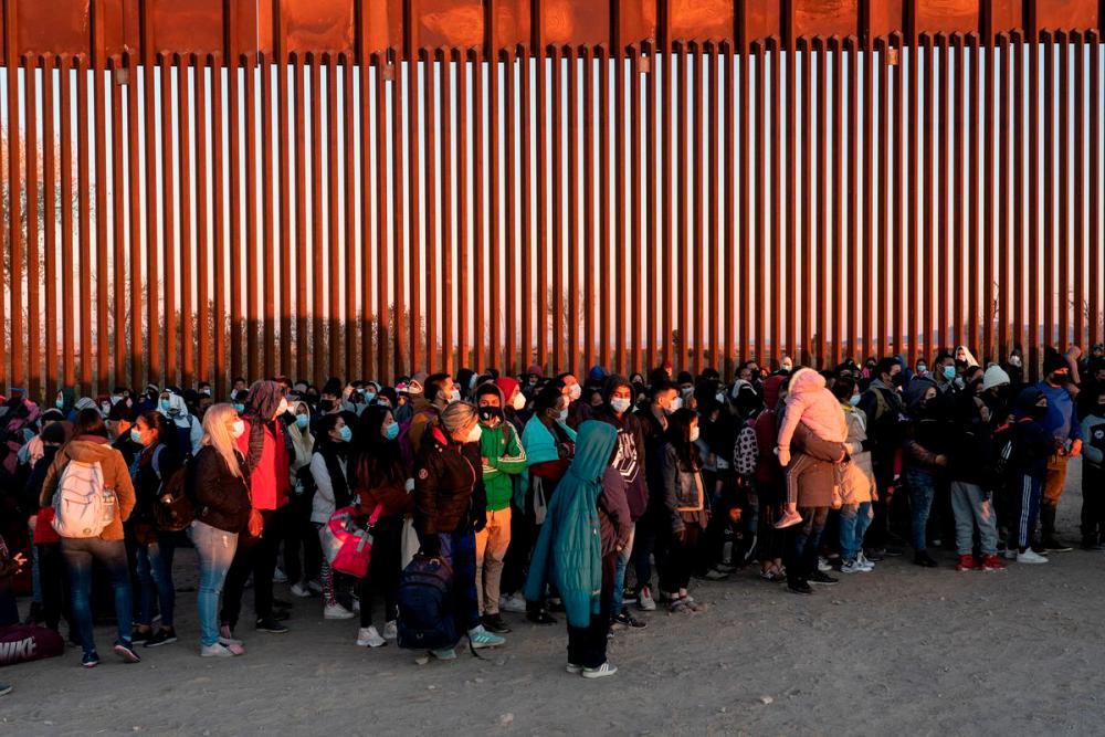 Migrants seeking asylum in the US, mostly from Venezuela, stand near the border fence while waiting to be processed by the US border patrol after crossing the border from Mexico at Yuma, Arizona, US, January 23, 2022. REUTERSPIX