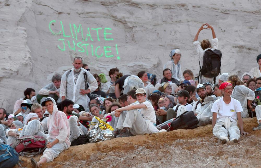 Climate activists sit on the ground after entering the Garzweiler brown coal mine in Garzweiler, western Germany, on June 22, 2019, during a weekend of massive protests in a growing climate civil disobedience movement. Anti-coal activists try to occupy the Garzweiler open-cast lignite mine in a protest to demand action against global warming, now one of the hottest issues on the European political agenda. — AFP