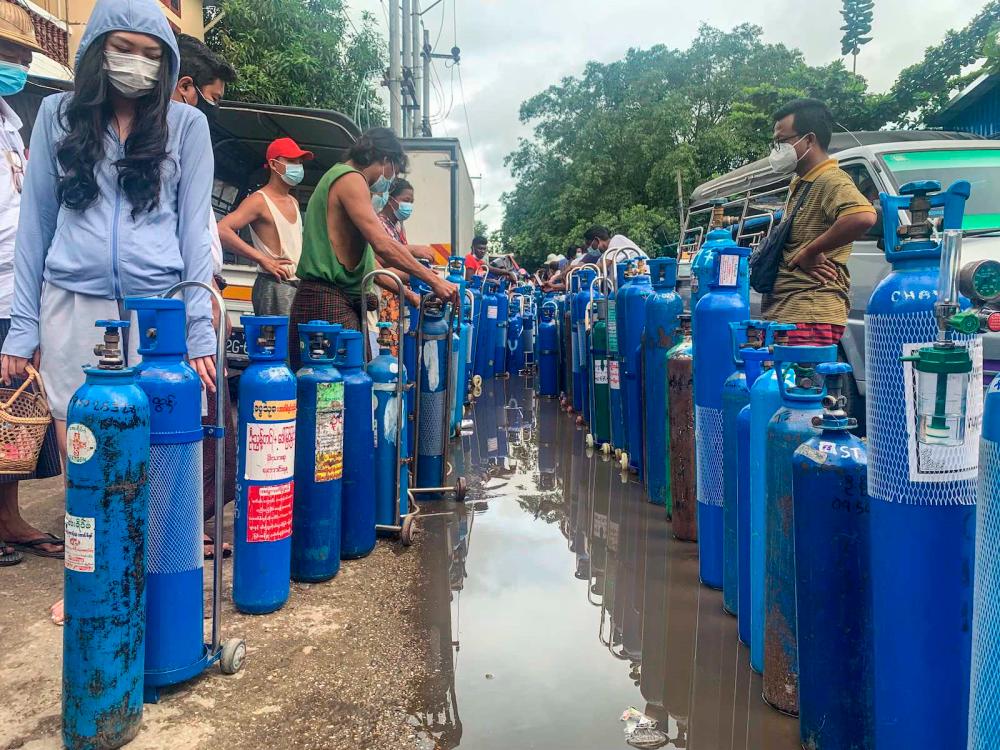 People stand with empty oxygen canisters as they wait to fill them up outside a factory in Yangon on 11 July - AFP via Getty images