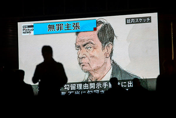 Photo of pedestrians passing by a television screen showing a news program displaying a sketch of former Nissan chief Carlos Ghosn in the courtroom, in Tokyo, as the headline reads in Japanese “Innocence claim.” — AFP