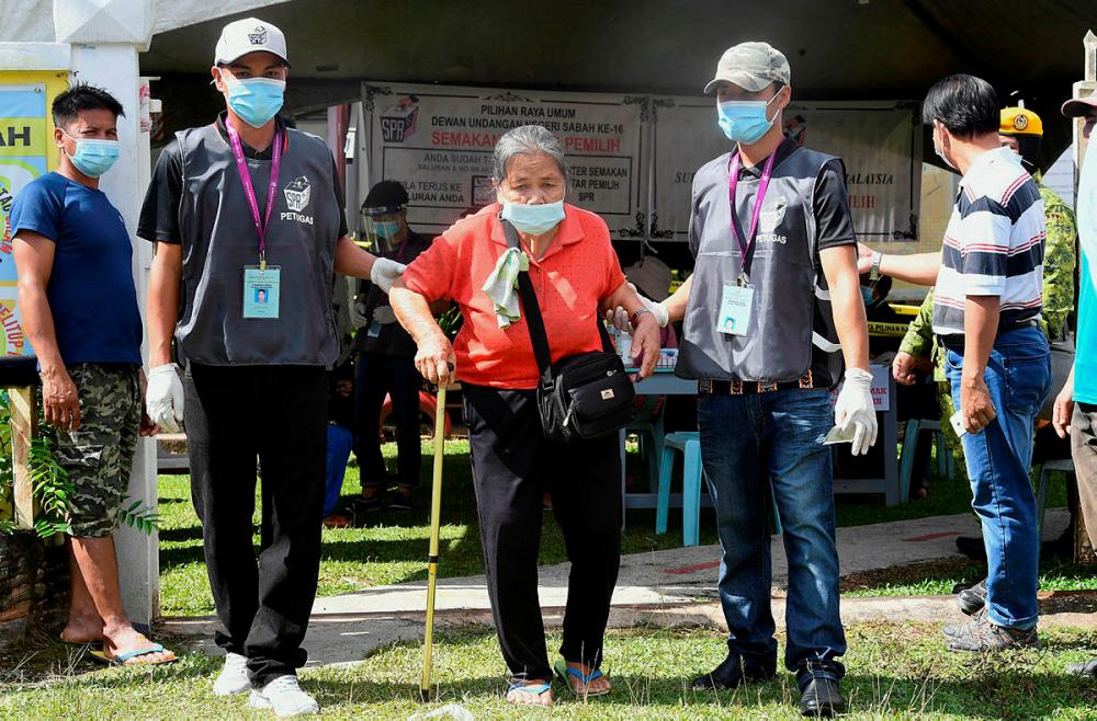 Election Commission staff helping an elderly person Gosiun Gumbala, 82, to cast her vote on the 16th Sabah State Election at Sekolah Kebangsaan Mantob today.-Bernama