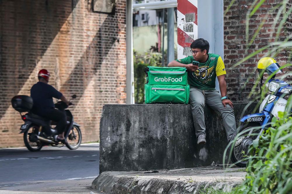 $!Modern communication has made it easier for people like Syamel to make ends meet as a food delivery rider and to communicate with his costumers by using his handphone. - ADIB RAWI YAHYA/THESUN