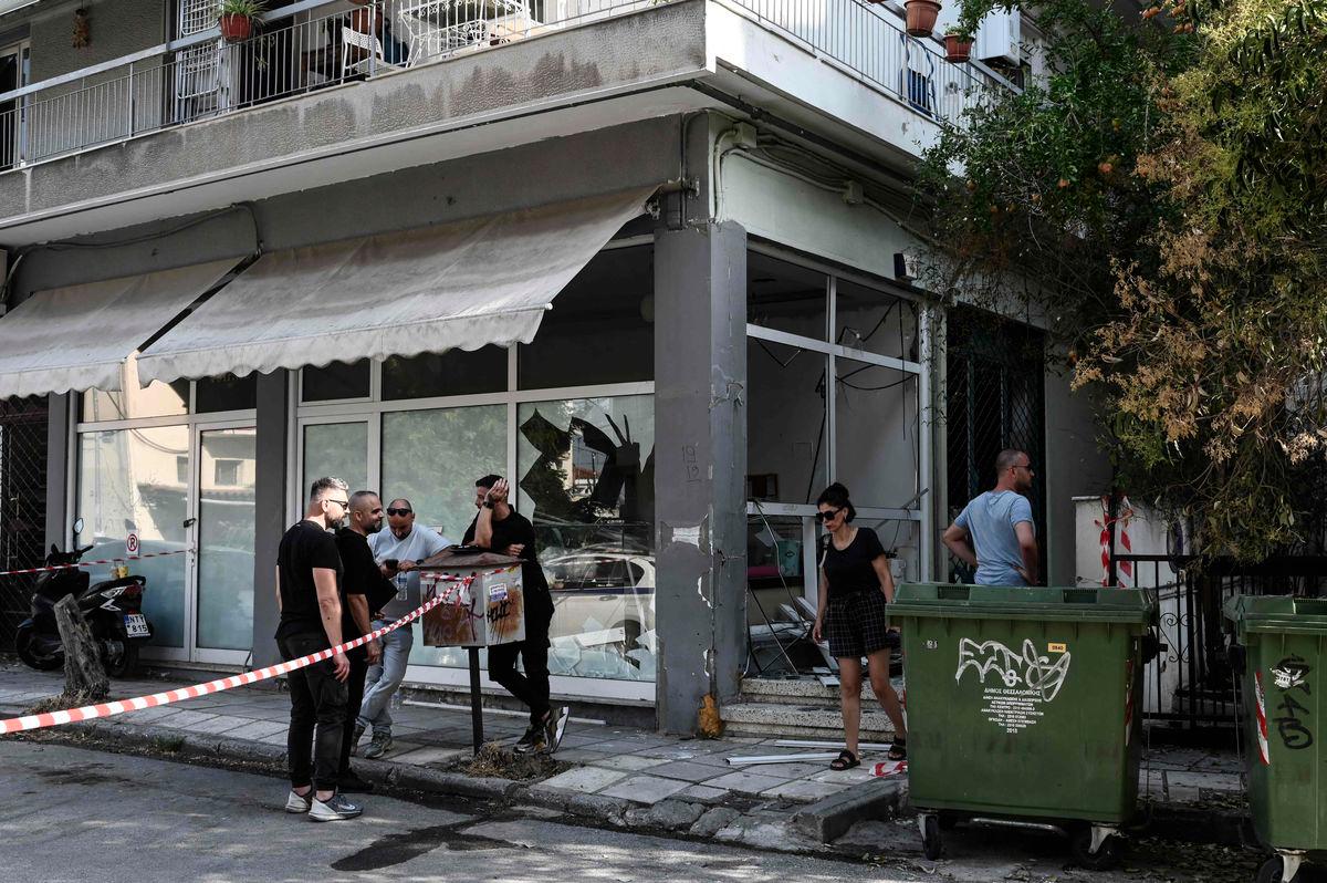 People stand next to a damaged shop following a strong blast in Thessaloniki on July 26, 2025. A strong blast early on July 26, 2025 damaged an apartment building in a suburb of Greece's second city Thessaloniki, wounding two passersby and shattering windows of nearby buildings. - AFPPIX