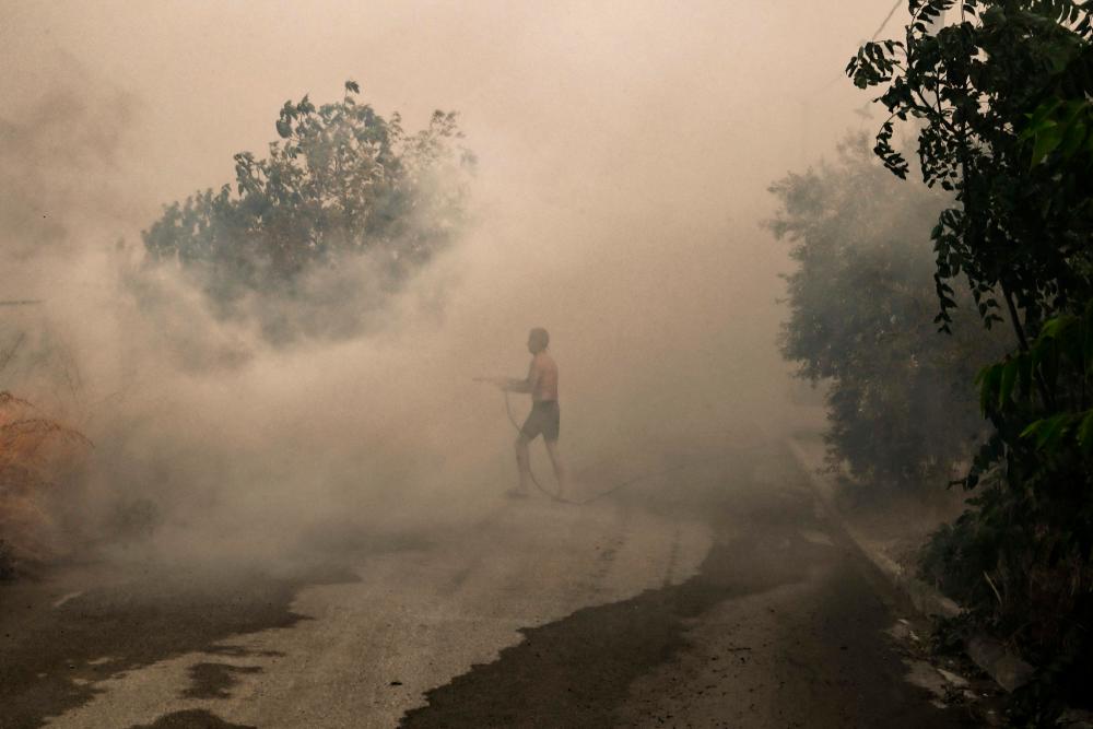 A local resident attempts to extinguish a fire in Nea Anchialos, near Greek mainland city of Volos, on July 27, 2023. Greek fire crews on July 27, 2023 scrambled to douse deadly wildfires raging for two weeks around the country//AFPix