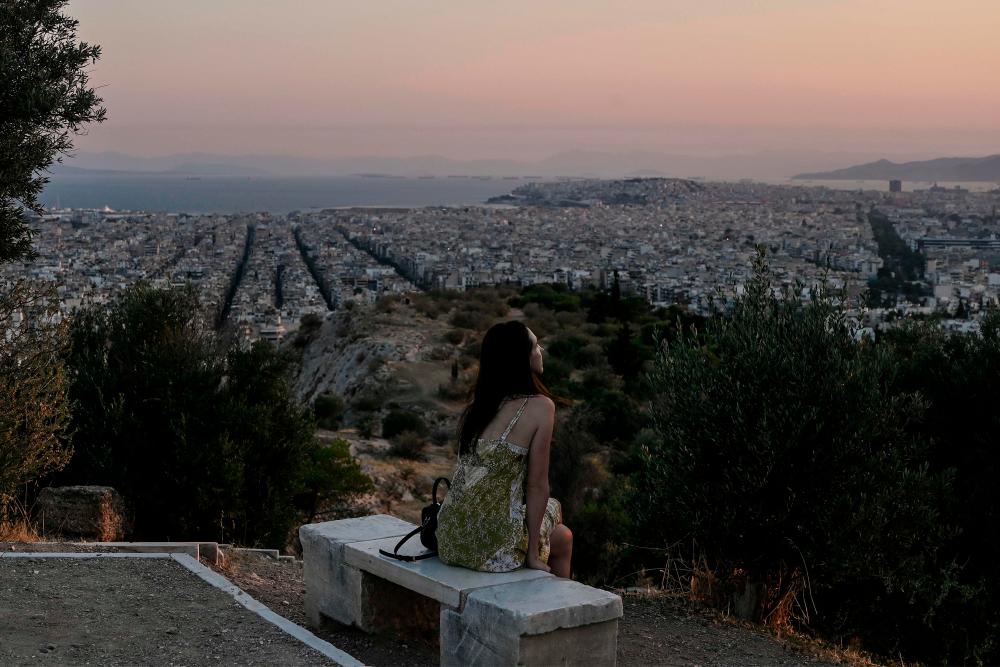$!A woman enjoys Athens cityscape on sunset on June 29, 2020 as tourists travelling to Greece will be required from July 1 to complete an online questionnaire 48 hours in advance to determine whether they need to be tested for coronavirus on arrival. / AFP / Louisa GOULIAMAKI