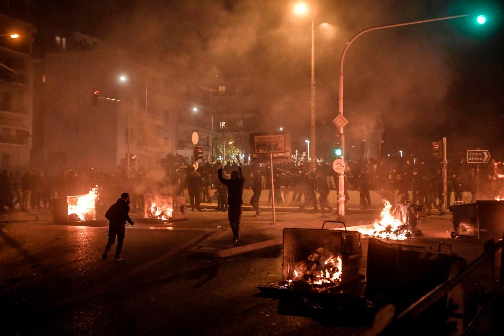 Protesters stand near burning trash bins during clashes with police at a demonstration against police violence in an Athens suburb on March 9, 2021. Greek police said an officer was seriously injured in the head as clashes broke out March 9 evening at a protest of some 5,000 people in Athens against police violence. The demonstration follows an uproar over viral video footage showing an officer beating a man with a baton during a patrol to check that people were following Covid-19 restrictions on March 7. — AFP
